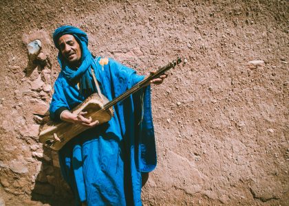 Afbeelding van een Gnaoua-man die traditionele muziek speelt in Essaouira, Marokko: ontdek de Gnaoua-cultuur tijdens uw autoverhuur in Fes.